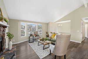 Living room featuring a stone fireplace, wood finished floors, a chandelier, and high vaulted ceiling