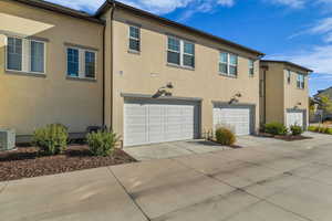 Rear view of house with an attached garage, stucco siding, and concrete driveway