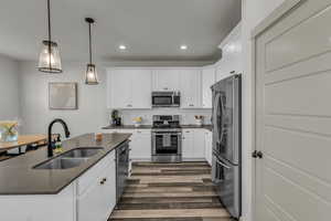 Kitchen featuring decorative backsplash, appliances with stainless steel finishes, hanging light fixtures, a center island with sink, and white cabinets