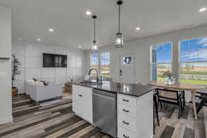 Kitchen featuring a center island with sink, dishwasher, a decorative wall, white cabinets, and recessed lighting