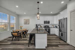 Kitchen featuring appliances with stainless steel finishes, decorative light fixtures, recessed lighting, a kitchen breakfast bar, and white cabinetry