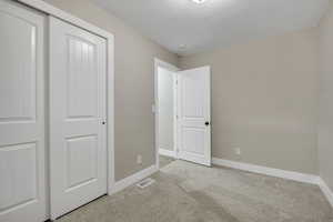 Unfurnished bedroom featuring carpet flooring, a textured ceiling, and a closet
