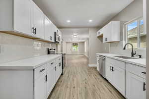 Kitchen with backsplash, stainless steel appliances, recessed lighting, light wood-style floors, and white cabinetry