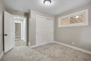 Unfurnished bedroom featuring light colored carpet, a closet, and a textured ceiling