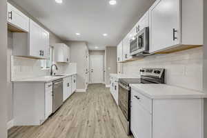 Kitchen featuring tasteful backsplash, stainless steel appliances, light wood finished floors, white cabinetry, and recessed lighting