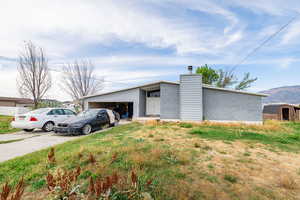 Mid-century inspired home featuring a chimney, an attached garage, concrete driveway, an outbuilding, and a mountain view