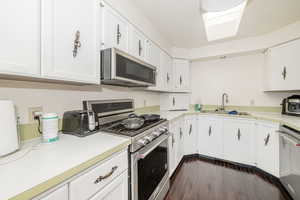 Kitchen featuring appliances with stainless steel finishes, light countertops, dark wood-style flooring, and white cabinetry