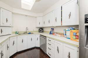 Kitchen with a skylight, light countertops, dark wood-style floors, and white cabinets