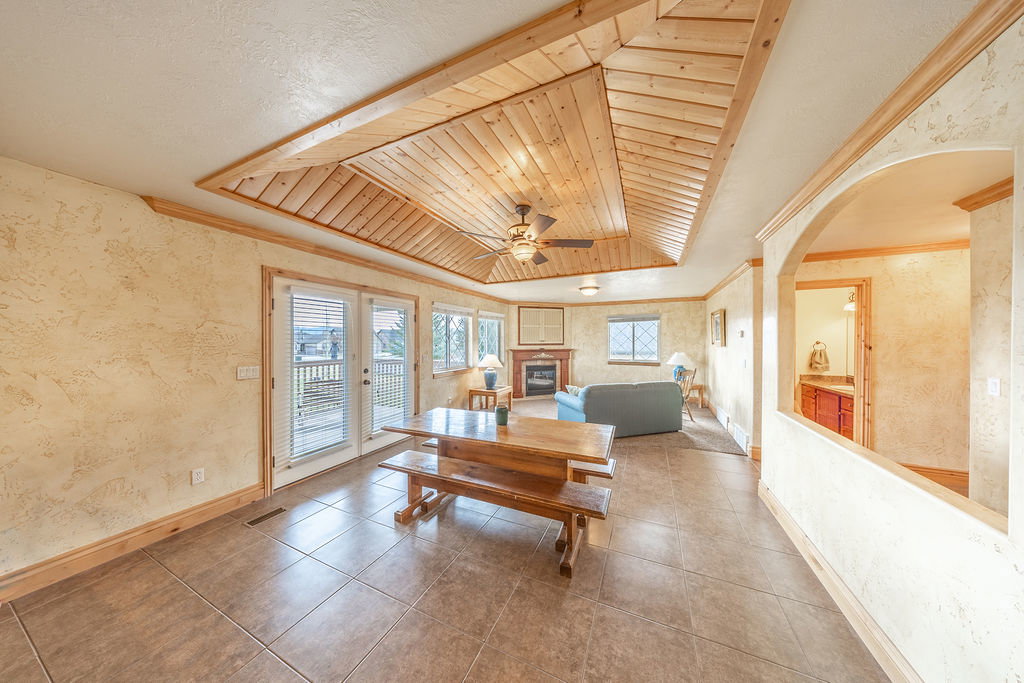 Dining space featuring wallpapered walls, a wooden tray ceiling, a ceiling fan, a glass covered fireplace, and arched walkways