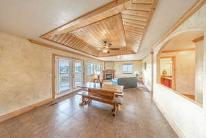 Dining space featuring wallpapered walls, a wooden tray ceiling, a ceiling fan, a glass covered fireplace, and arched walkways