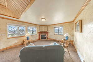 Carpeted living room with a fireplace, cooling unit, a textured wall, crown molding, and vaulted ceiling