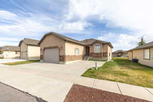 Ranch-style home featuring a garage, driveway, stucco siding, a front yard, and stone siding