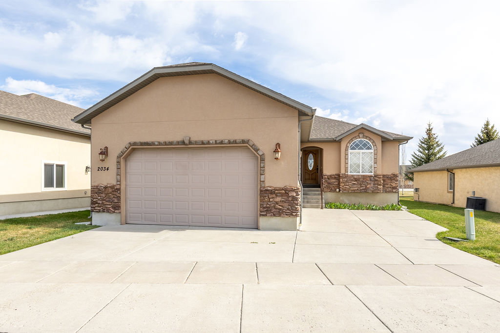 Ranch-style home with stucco siding, a garage, concrete driveway, and stone siding