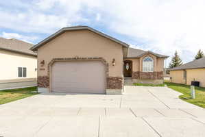 Ranch-style home with stucco siding, a garage, concrete driveway, and stone siding