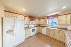 Kitchen featuring white appliances, cream cabinetry, glass fronted cabinets, light countertops, and light tile patterned floors