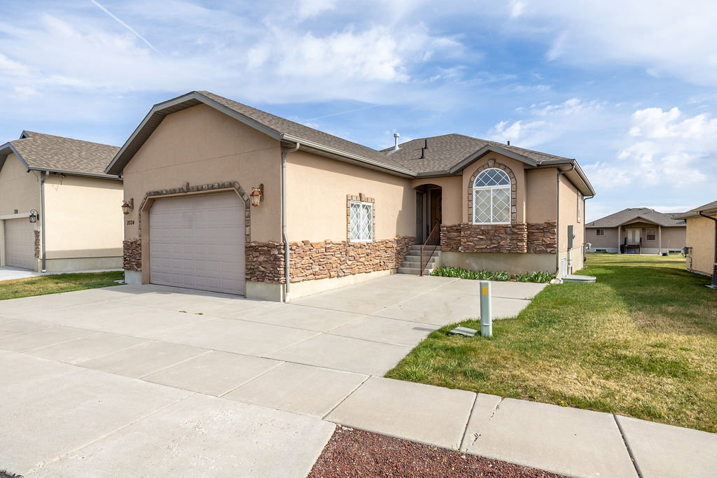 Single story home featuring stucco siding, a garage, concrete driveway, a front lawn, and stone siding