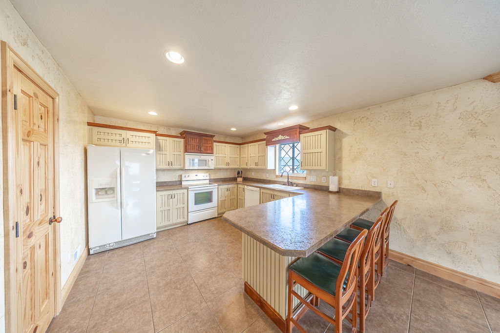 Kitchen featuring white appliances, a peninsula, a breakfast bar area, glass fronted cabinets, and dark countertops