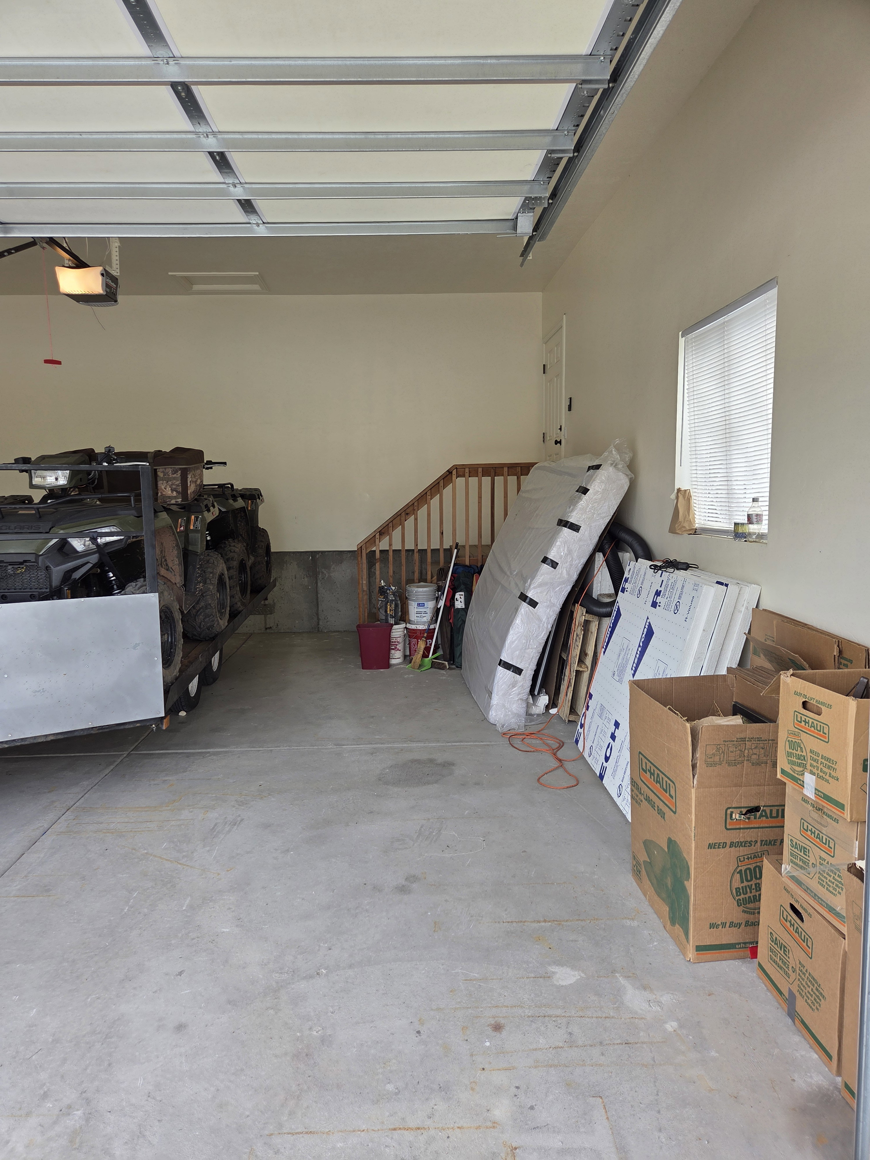 Garage space featuring concrete flooring, an overhead door with visible track system, painted walls, and a window with blinds