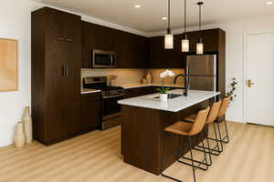 Kitchen featuring backsplash, appliances with stainless steel finishes, modern cabinets, dark brown cabinetry, and a kitchen bar