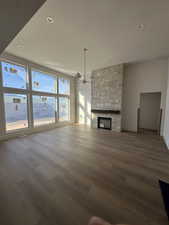 Unfurnished living room with a stone fireplace, dark wood finished floors, and hanging lights