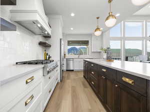 Dual tone kitchen with light wood finished floors, two tone cabinets, stainless steel appliances, decorative light fixtures, and open shelves