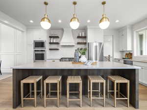 Kitchen with open shelves, a breakfast bar, light wood-type flooring, stainless steel appliances, and dual tone cabinetry