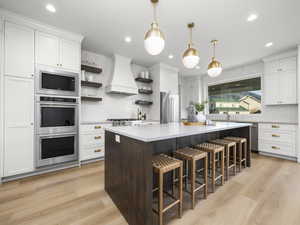 Kitchen with open shelves, a kitchen island, a kitchen breakfast bar, two tone color scheme, and light wood finished floors