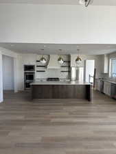 Kitchen featuring open shelves, pendant lighting, stainless steel appliances, light wood-style floors, and a spacious island