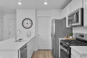 Kitchen with a peninsula, appliances with stainless steel finishes, light wood-type flooring, white cabinetry, and recessed lighting