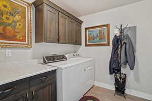Washroom with cabinet space, light wood-type flooring, a textured ceiling, independent washer and dryer, and electric panel