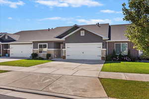 View of front of property featuring stone siding, concrete driveway, a shingled roof, and a front lawn