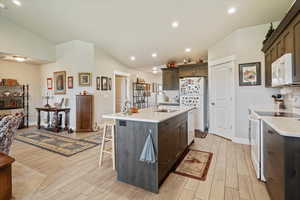 Kitchen featuring dark brown cabinets, white appliances, light wood finished floors, a kitchen bar, and recessed lighting