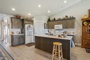 Kitchen with white appliances, vaulted ceiling, wood tiled floors, decorative backsplash, and dark brown cabinets