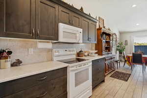 Kitchen with white appliances, tasteful backsplash, dark brown cabinets, quartz counter tops, and wood finish floors