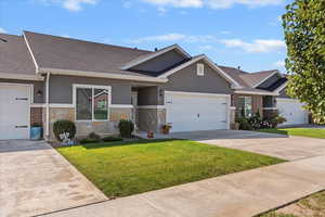 Single story home featuring stucco siding, roof with shingles, a front lawn, and stone siding