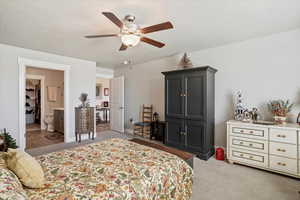 Bedroom featuring light colored carpet, a textured ceiling, ceiling fan, and ensuite bath