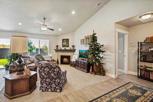 Living area featuring lofted ceiling, wood tiled floors, a ceiling fan, recessed lighting, and a lit fireplace