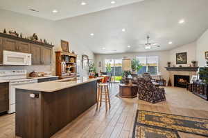 Kitchen featuring white appliances, open floor plan, lofted ceiling, dark brown cabinetry, and light wood finished floors
