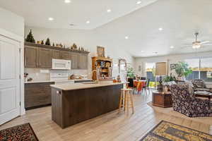 Kitchen featuring white appliances, backsplash, vaulted ceiling, open floor plan, and light wood-type flooring