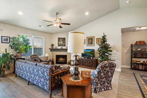 Living room featuring wood tiled floors, lofted ceiling, a lit fireplace, ceiling fan, and recessed lighting