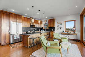 Kitchen featuring brown cabinetry, stainless steel appliances, dark countertops, tasteful backsplash, and a breakfast bar area