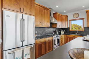Kitchen with stainless steel appliances, brown cabinetry, backsplash, wall chimney range hood, and recessed lighting