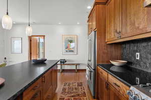 Kitchen featuring brown cabinetry, light wood-type flooring, backsplash, hanging light fixtures, and recessed lighting