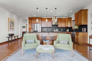 Kitchen featuring wood finished floors, decorative light fixtures, backsplash, wall chimney exhaust hood, and recessed lighting