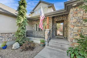 Doorway to property featuring stone siding, stucco siding, and covered porch