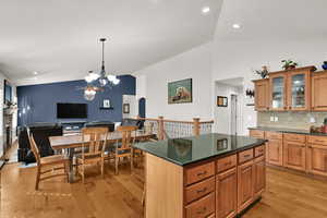 Kitchen with vaulted ceiling, a chandelier, brown cabinetry, a kitchen island, and light wood-type flooring
