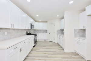 Kitchen with white cabinets, stainless steel appliances, decorative backsplash, recessed lighting, and light wood-type flooring