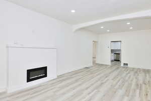 Unfurnished living room with recessed lighting, a glass covered fireplace, light wood-style flooring, and arched walkways