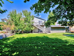 View of grassy yard with stairs, a patio, and a deck