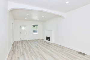 Unfurnished living room featuring recessed lighting, light wood finished floors, a glass covered fireplace, and arched walkways